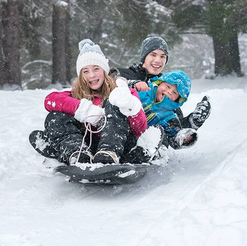 Three children sliding down a snow toboggan hill at Manning Park Resort.