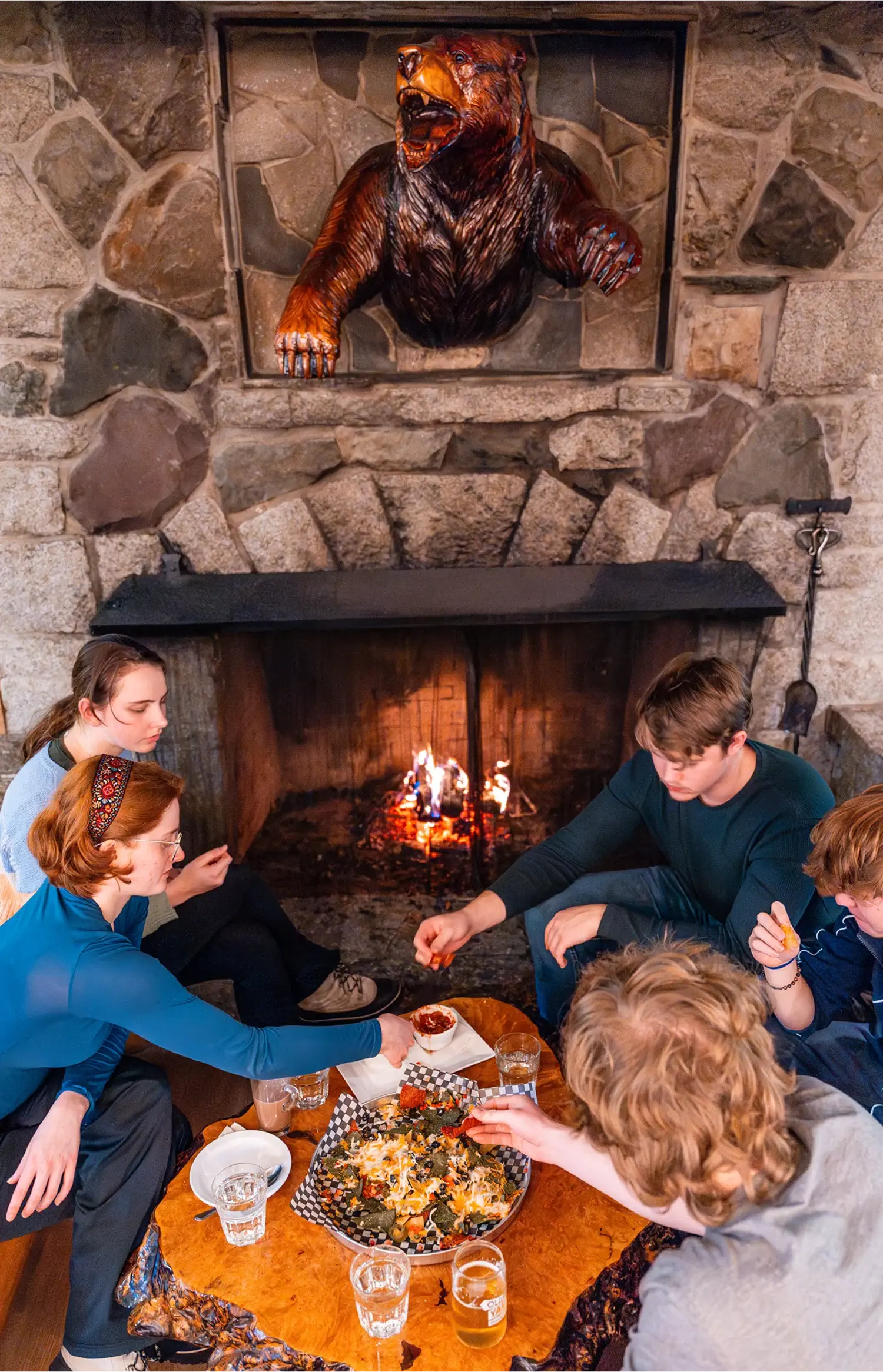 Group enjoying a meal together in front of a cozy fireplace at the Bear’s Den Pub.