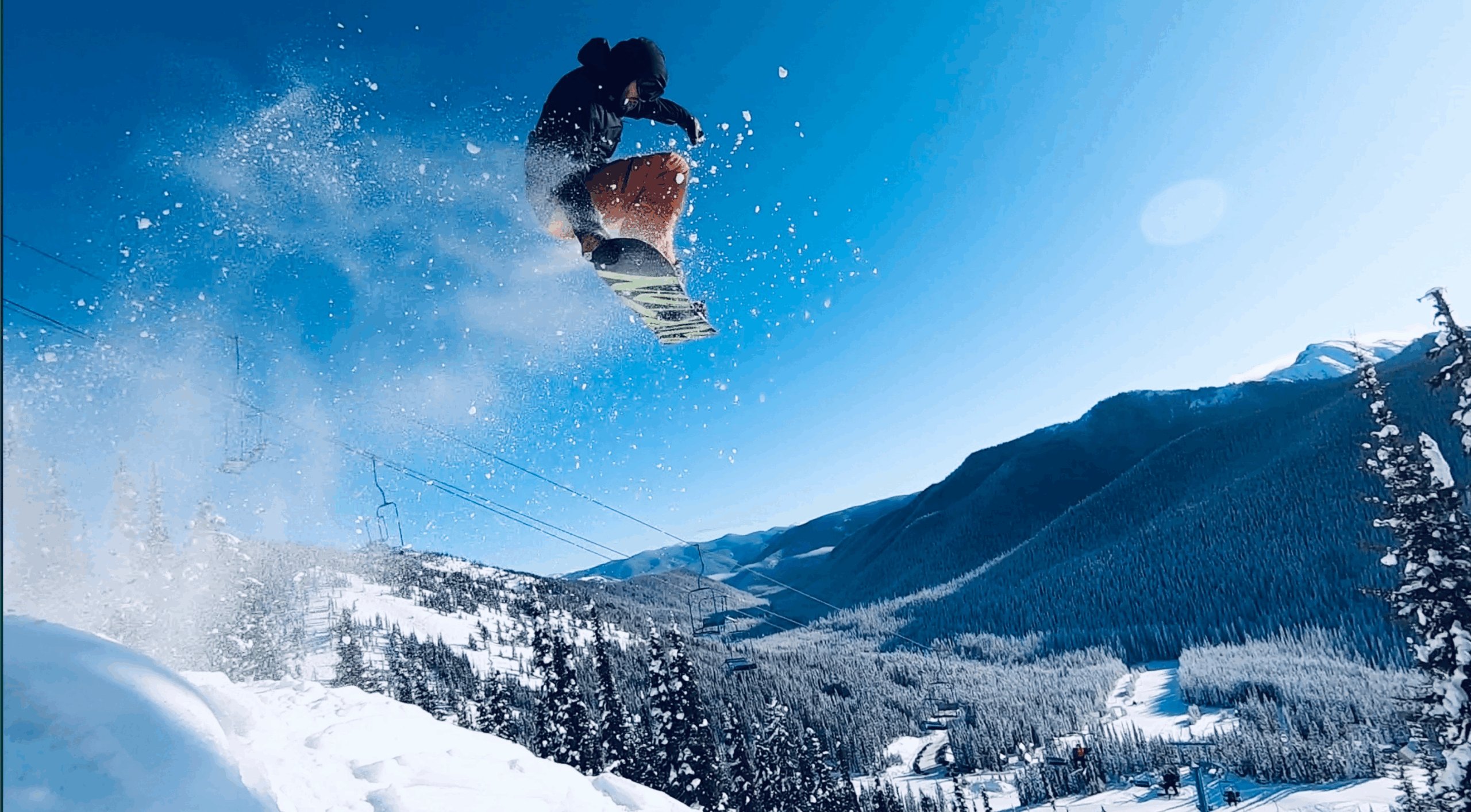 Snowboarder performing a jump against a snowy mountain backdrop at the Alpine in Manning Park.